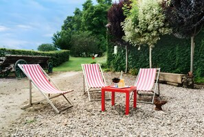 A gravel patio with two striped lounge chairs and a small red table.