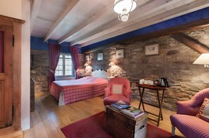 Quarto com cama, duas cadeiras, uma mesa e parede de pedra.