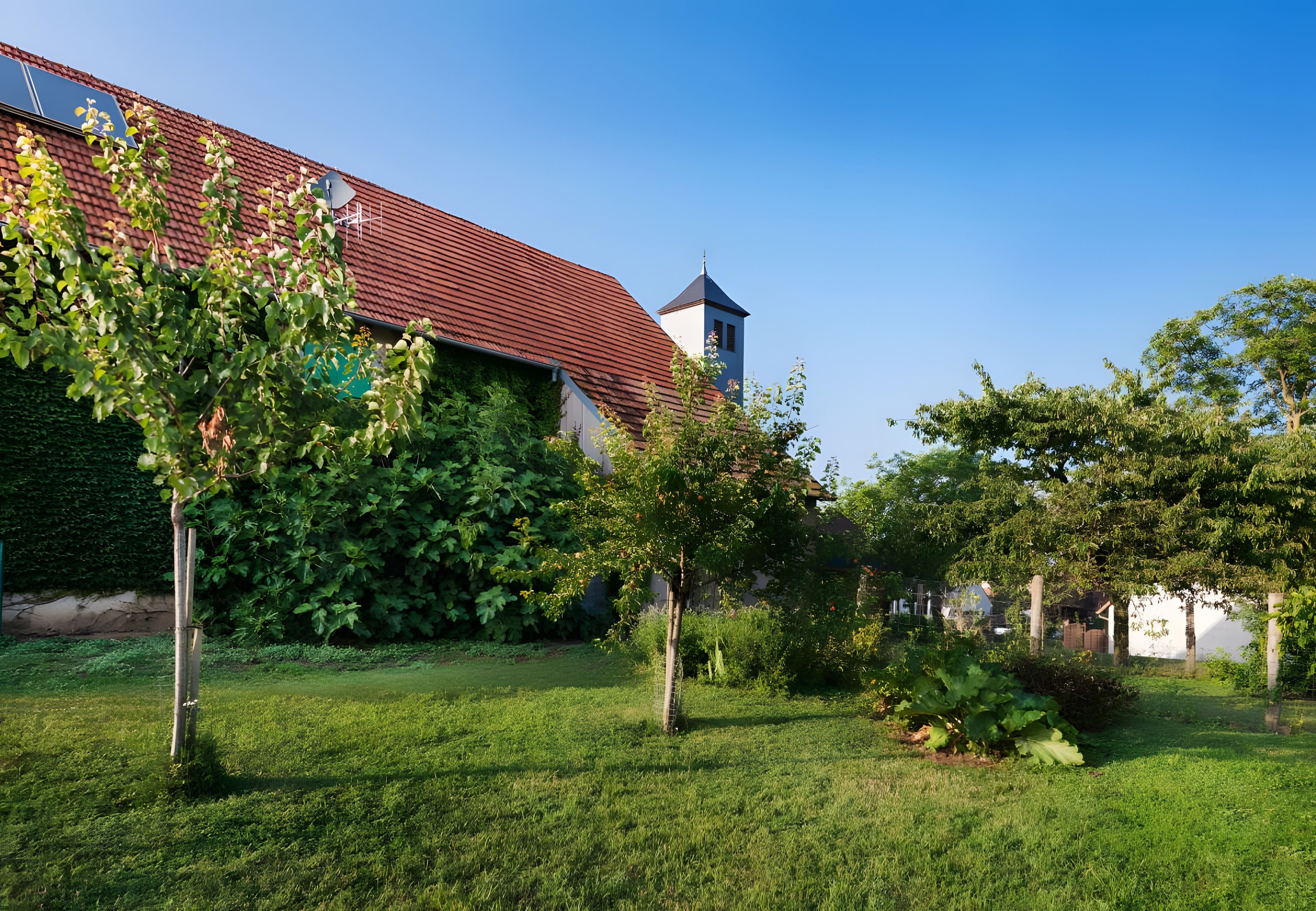 A building with a red roof, surrounded by a well-maintained garden with various trees and shrubs.