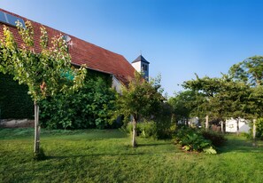 A building with a red roof, surrounded by a well-maintained garden with various trees and shrubs.