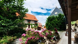 Une cour intérieure avec un bâtiment de style traditionnel, un chemin pavé et des plantes en fleurs.