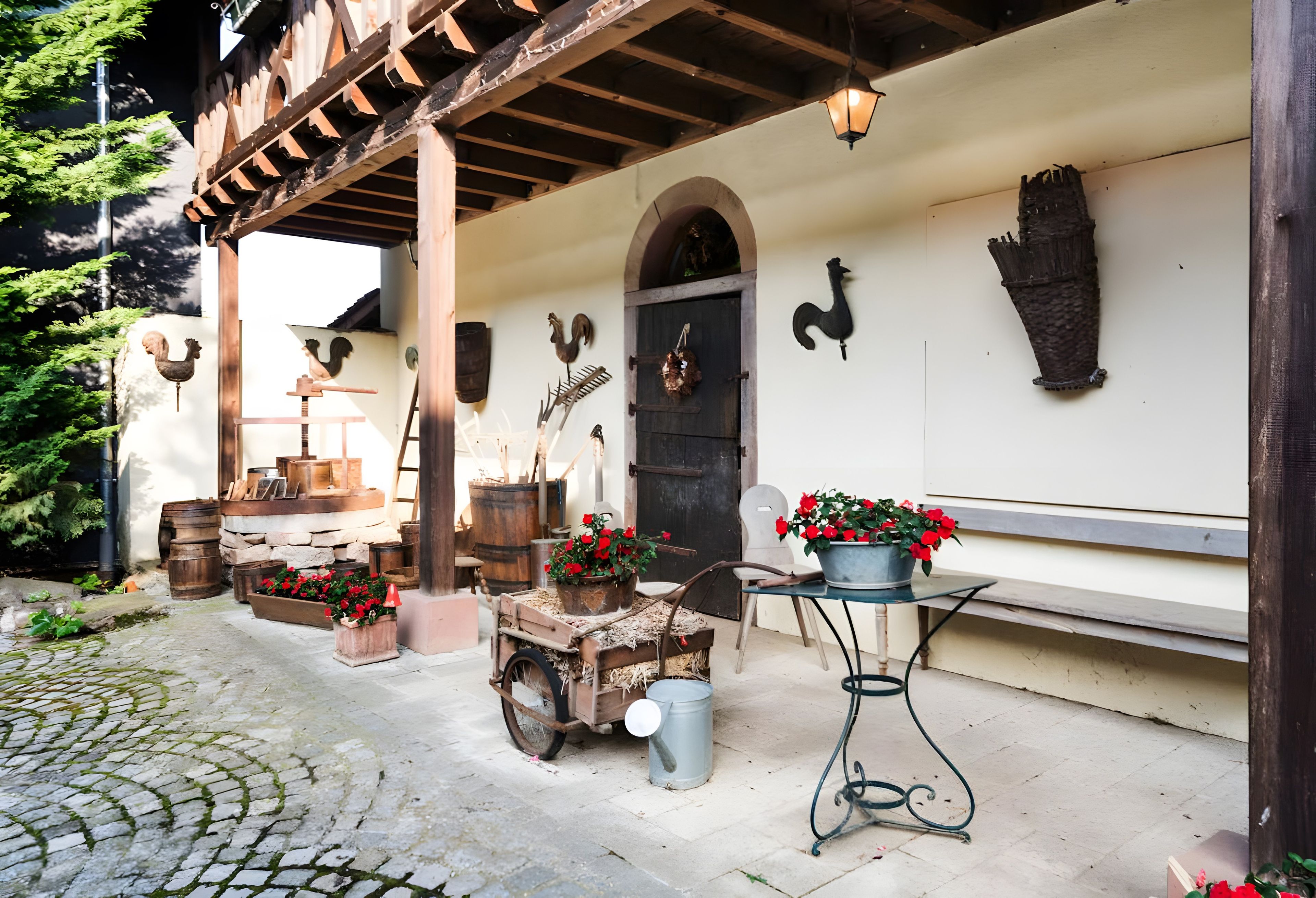 A rustic outdoor setting with a wooden structure, a stone bench, a wheelbarrow with firewood, and a potted plant.