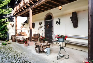 A rustic outdoor setting with a wooden structure, a stone bench, a wheelbarrow with firewood, and a potted plant.