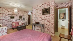 Une pièce avec un papier peint à motifs floraux, un lit, un canapé, une petite table et une porte donnant sur une autre pièce.