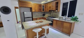 A modern kitchen with wooden cabinets, granite countertops, a stainless steel refrigerator, and a gas stove. - Villa La Escapada - Private Caribbean Oasis Near Juan Dolio Beach (San Pedro de Macorís)