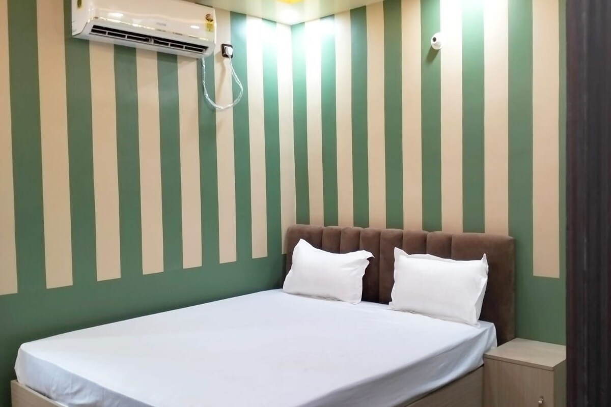 Una habitación de hotel con cama, cabecero, mesita de noche y aire acondicionado en la pared.