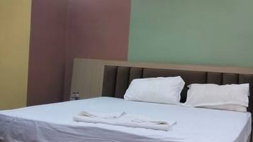A hotel room with a bed, a ceiling fan, an air conditioning unit, and a wall-mounted light fixture.
