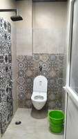 A small bathroom with a toilet, a shower, and a green bucket.