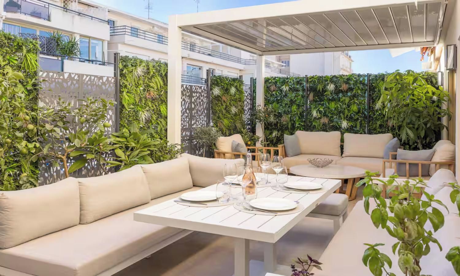 An outdoor patio with a white table set for dining, surrounded by beige sofas and a covered seating area.