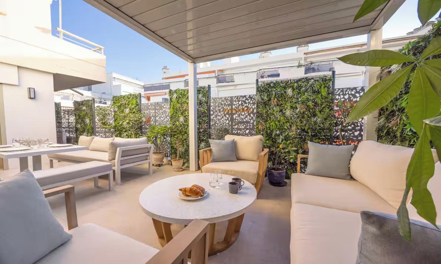 Un área de estar al aire libre con una mesa redonda, sillas acolchadas y plantas en macetas.
