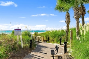 A beach path with a warning sign, a bench, and a view of the ocean. - Grand Panama 2-104 | 2BR + Bunks | Sleeps 7 (Panama City Beach)