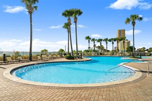 A swimming pool with palm trees, lounge chairs, and a building in the background. - Grand Panama 2-104 | 2BR + Bunks | Sleeps 7 (Panama City Beach)