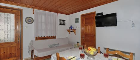 Un comedor con una mesa de madera dispuesta para dos personas, un televisor montado en la pared y una puerta de madera.