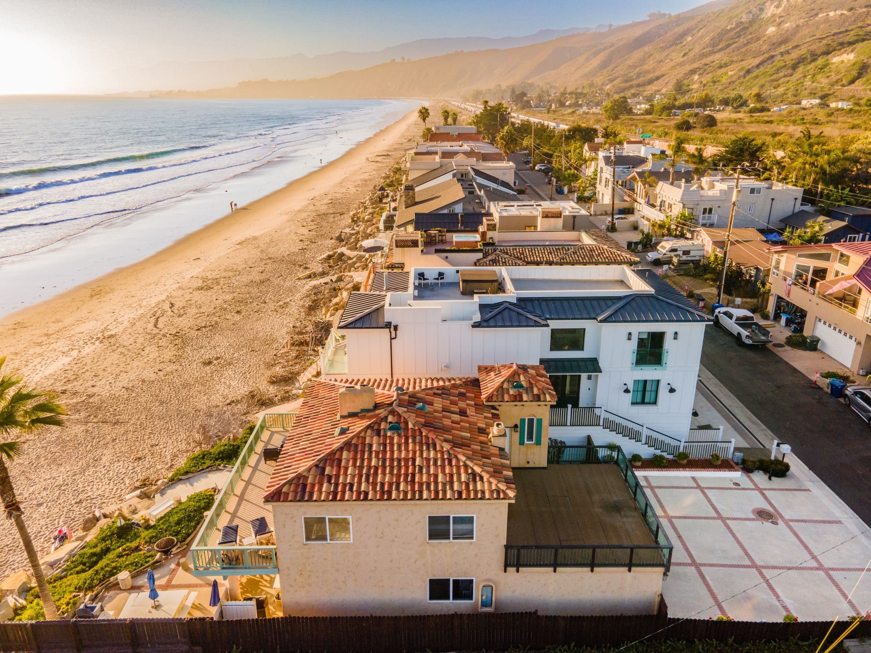 A coastal residential area with houses, a beach, and a hilly landscape in the background.