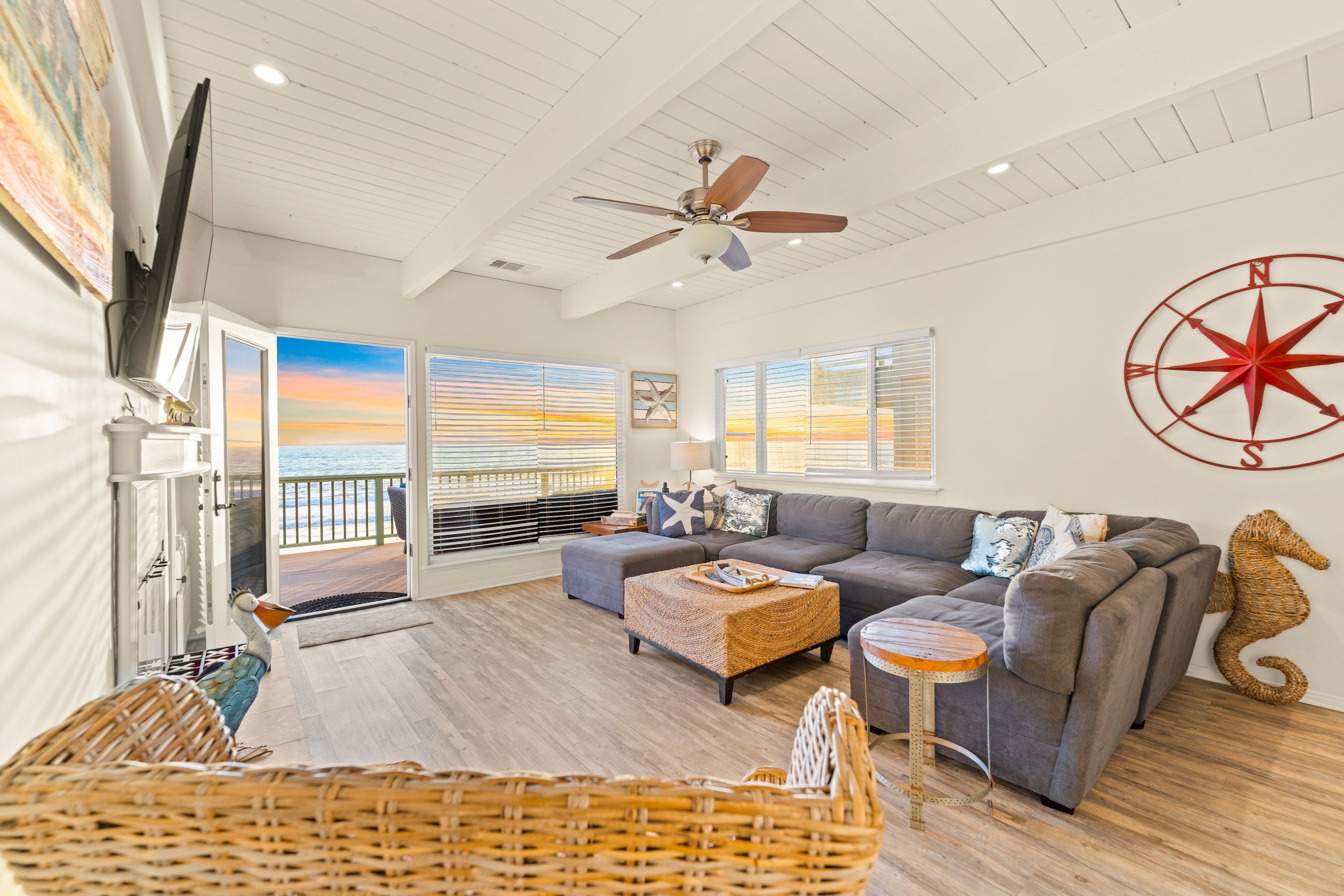 A spacious living room with a large gray sofa, a wooden coffee table, and a view of the beach through the windows.
