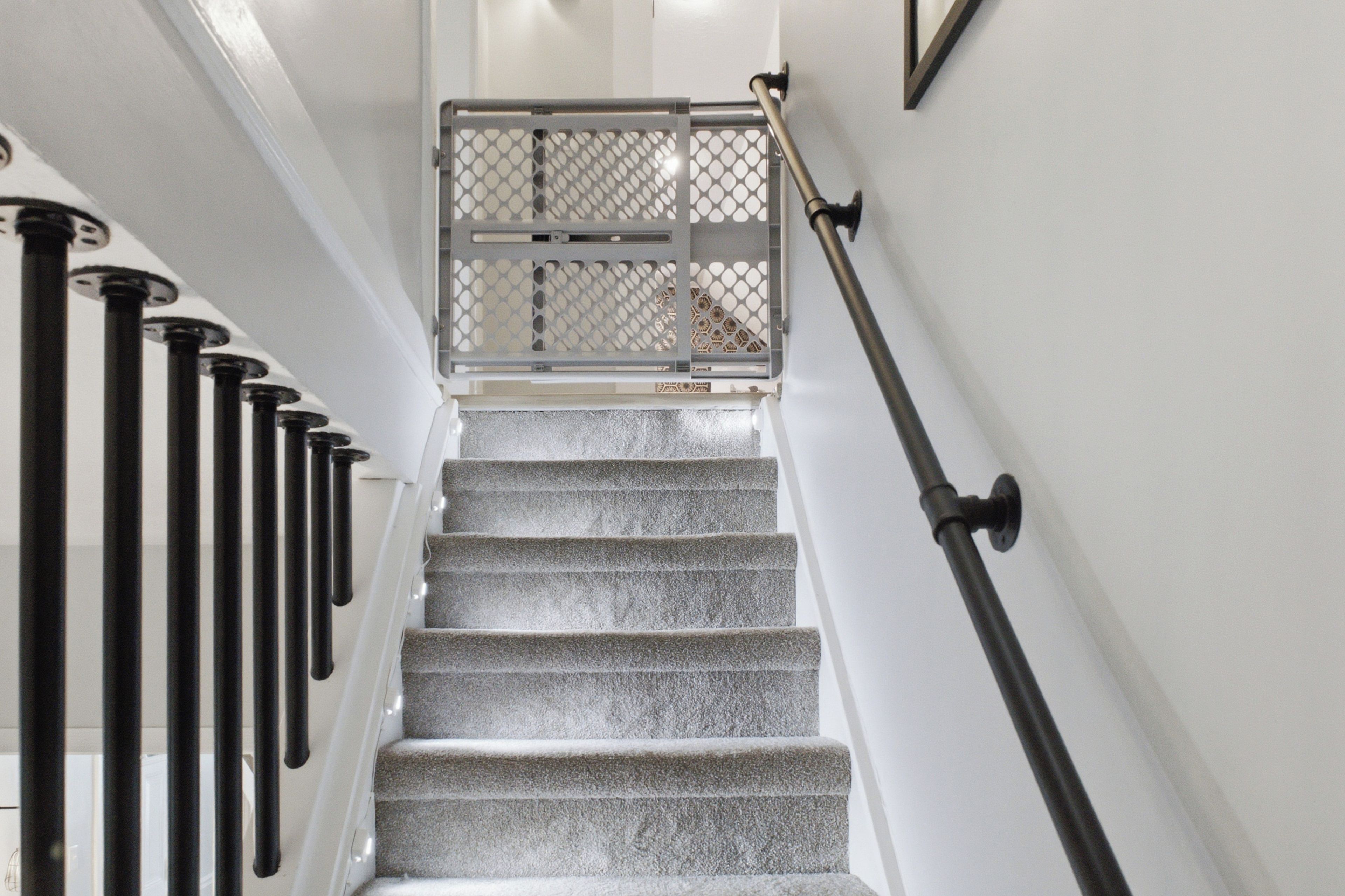 Una escalera con barandilla de metal, balaustrada de vidrio y pared blanca.