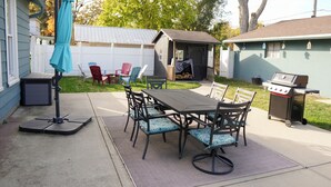 En udendørs terrasse med et bord, stole, grill og et overdækket område med stole.