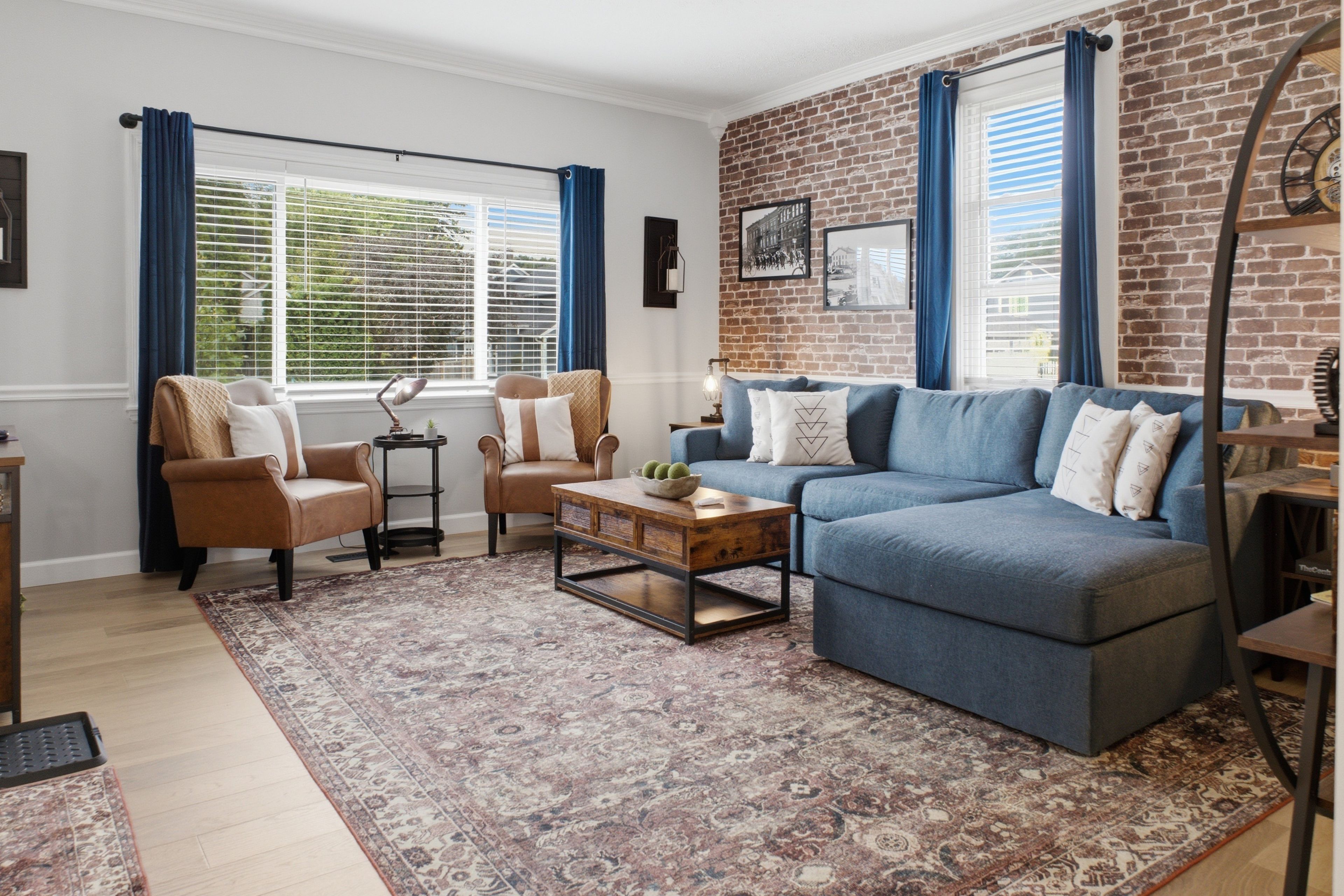 Ein Wohnzimmer mit blauem Sofa, zwei Sesseln, einem Couchtisch und einem gemusterten Teppich.