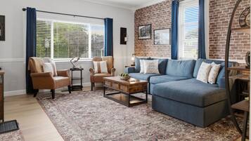 Ein Wohnzimmer mit blauem Sofa, zwei Sesseln, einem Couchtisch und einem gemusterten Teppich.