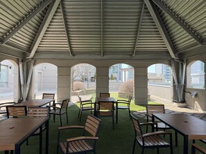 Eine überdachte Terrasse im Freien mit Tischen und Stühlen, bogenförmigen Durchgängen und Blick auf die Umgebung.