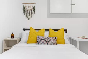 A bed with white bedding, two yellow pillows, and a patterned pillow. There is a bottle on a bedside table and a wall hanging above the bed. - Bright 2BR Stay • Near Bus Stop • Free Parking (Toronto)