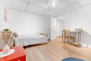 Ein Schlafzimmer mit einem Bett, einem Schreibtisch mit Stuhl, einem roten Tisch und einer Vase mit getrockneten Blumen.