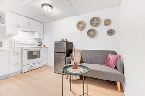 Eine kompakte Küche mit weißen Schränken, einem Kühlschrank und einem Essbereich mit Tisch und Sofa.