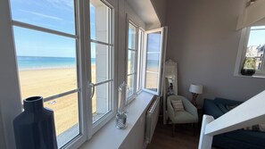 Ein Zimmer mit Blick auf den Strand, ein Sessel, eine Lampe und eine Vase auf der Fensterbank.