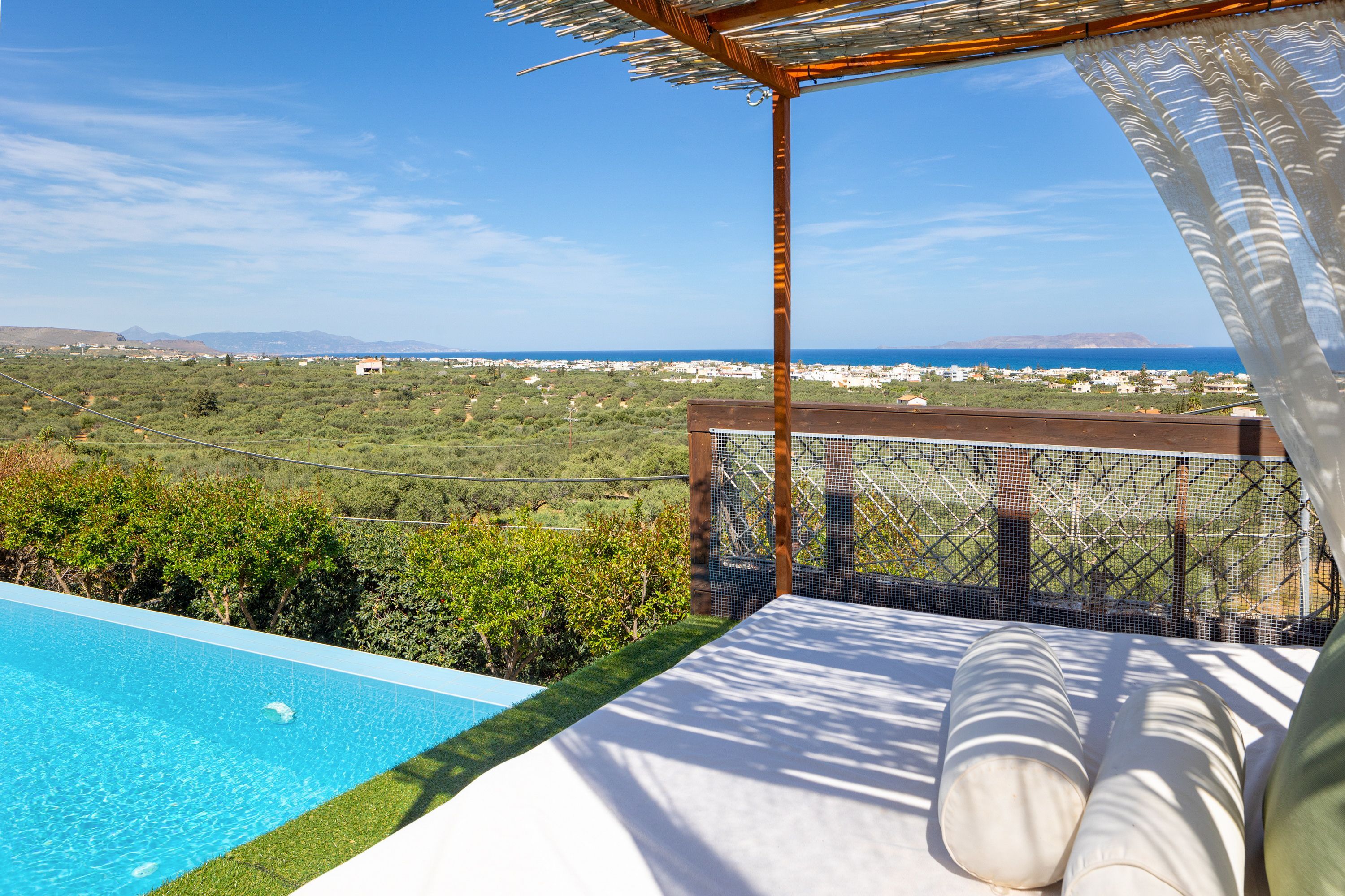 A poolside area with a view of the sea and a distant cityscape.