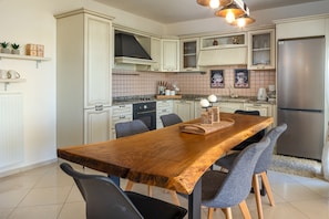 A kitchen with a wooden dining table, chairs, a refrigerator, and various kitchen appliances. - Villa Konstantinos in Heraklion (Hersonissos)