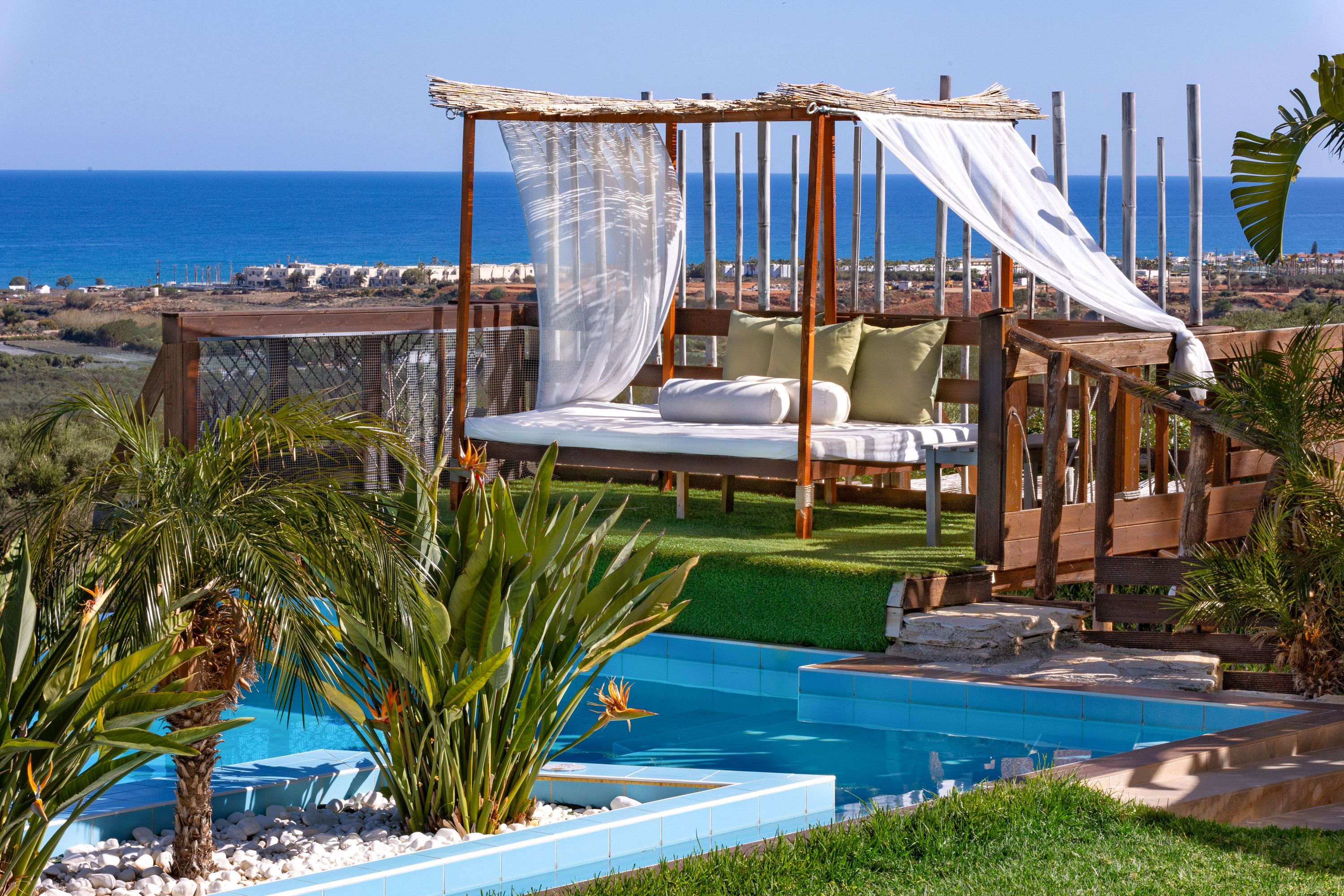 A beachside pool area with a canopy bed overlooking the sea.