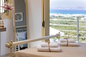 A room with a bed, a window with a view of the sea, and a towel rack with towels. - Villa Konstantinos in Heraklion (Hersonissos)