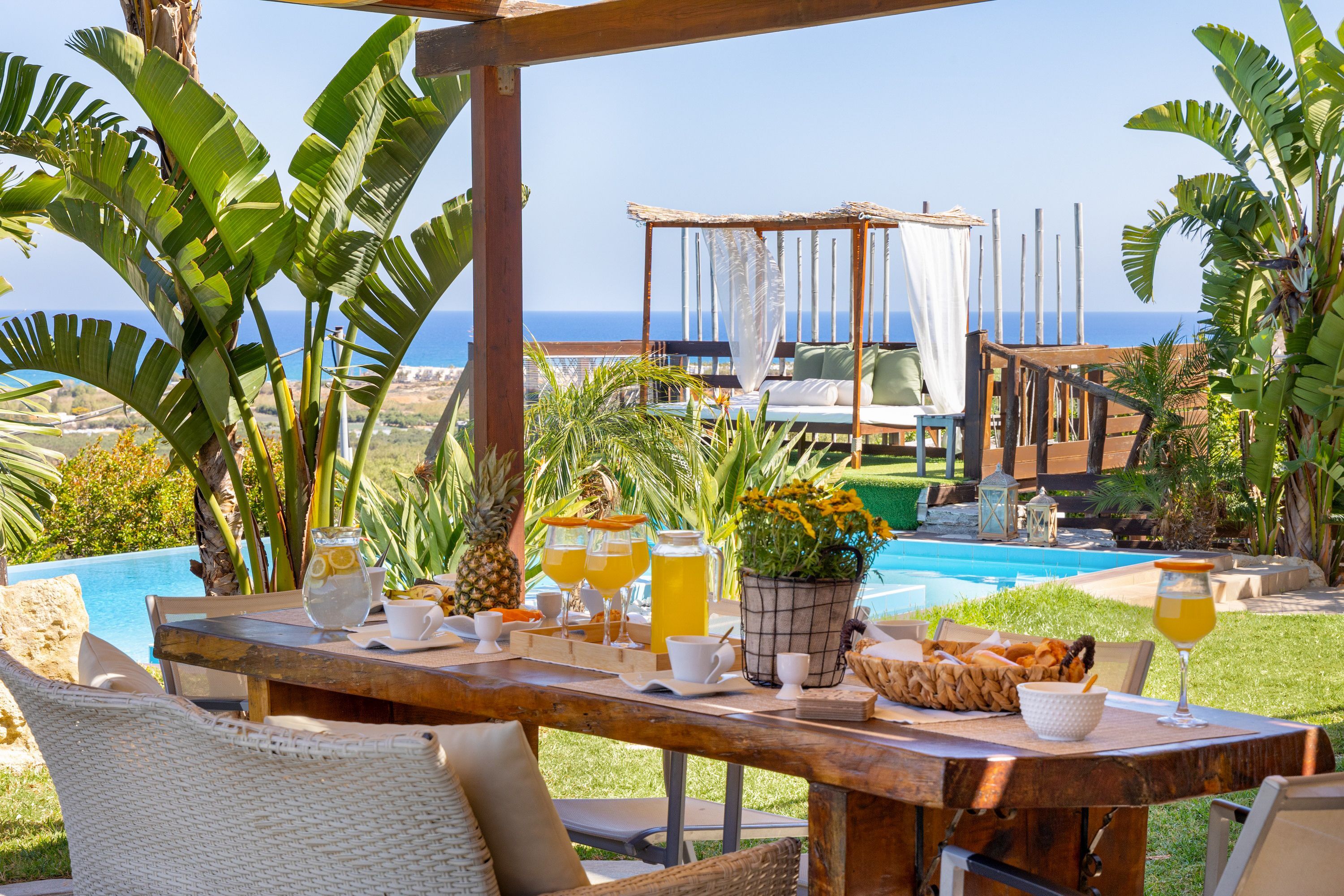 Un espace extérieur aménagé pour les repas, avec une piscine, des plantes tropicales et une vue sur l’océan.