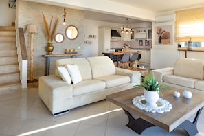 A modern living room with a sofa, a coffee table with a plant, and a kitchen in the background. - Villa Konstantinos in Heraklion (Hersonissos)
