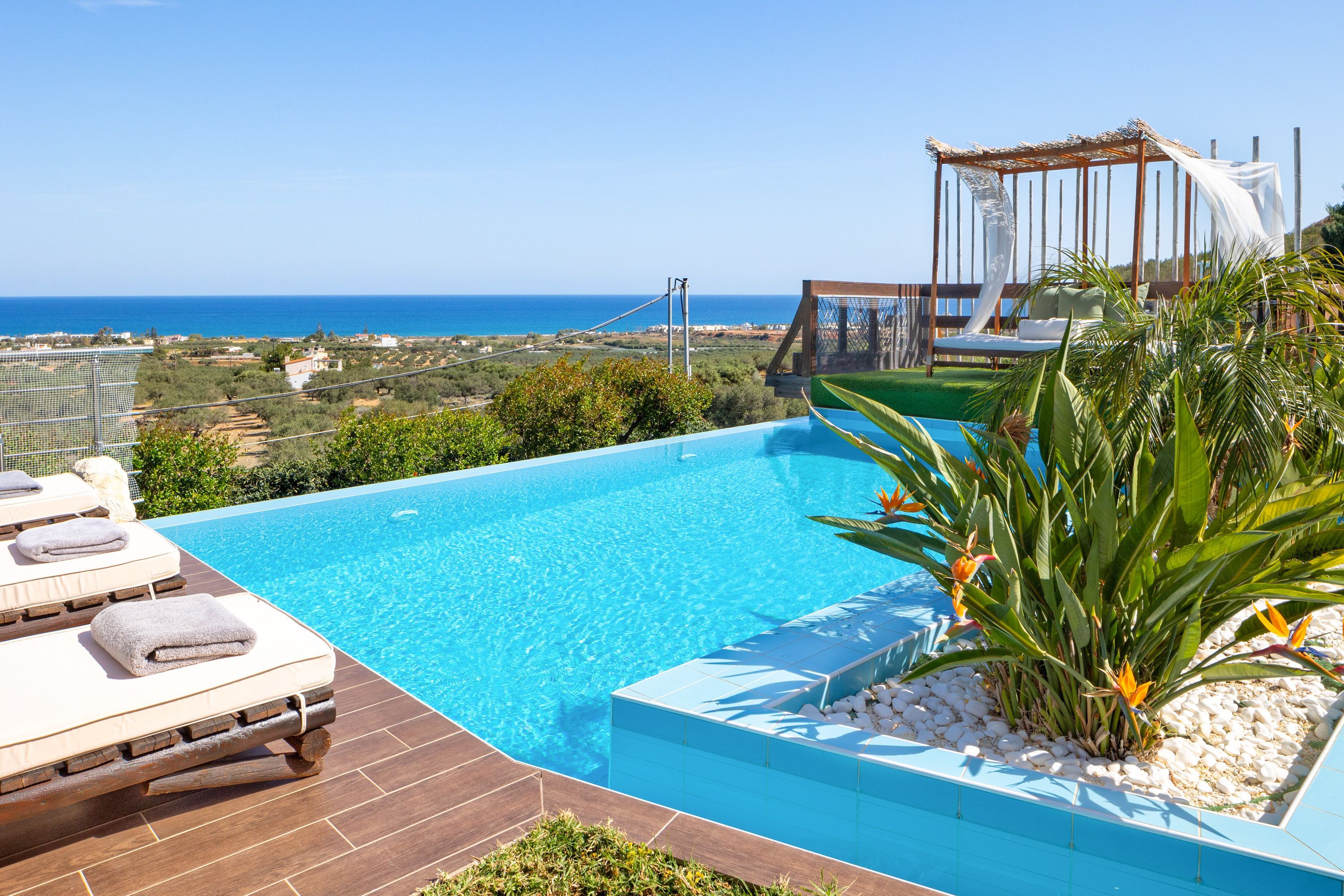 A pool with a view of the sea, lounge chairs, and a pergola.