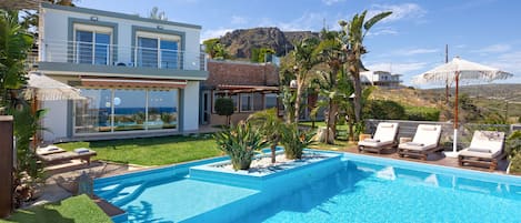A modern two-story house with a swimming pool, outdoor seating, and a view of a mountain.