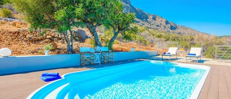 A swimming pool with a wooden deck, lounge chairs, and a mountain backdrop.