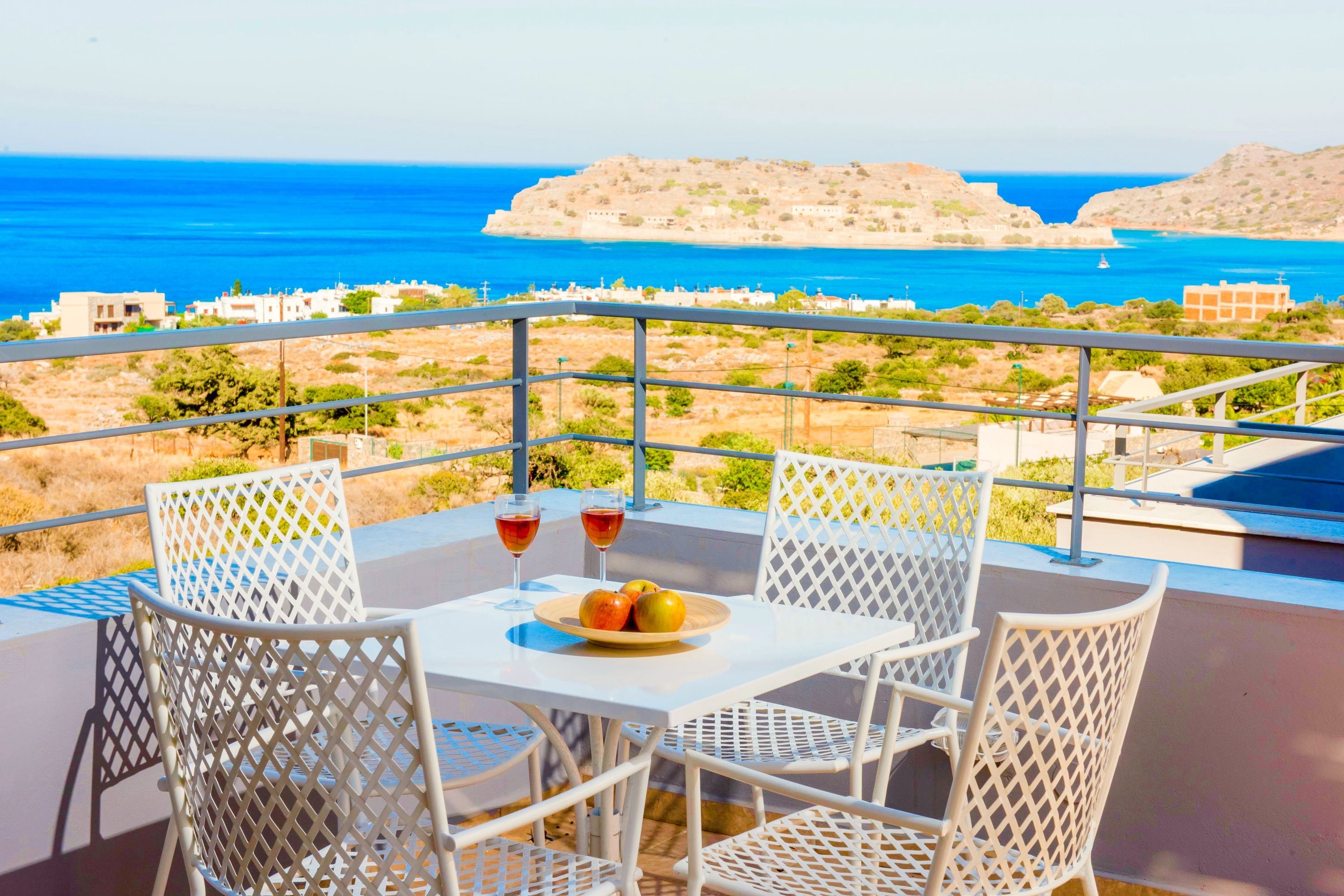 Un balcon avec une table, deux chaises et une vue sur la mer et les bâtiments éloignés.