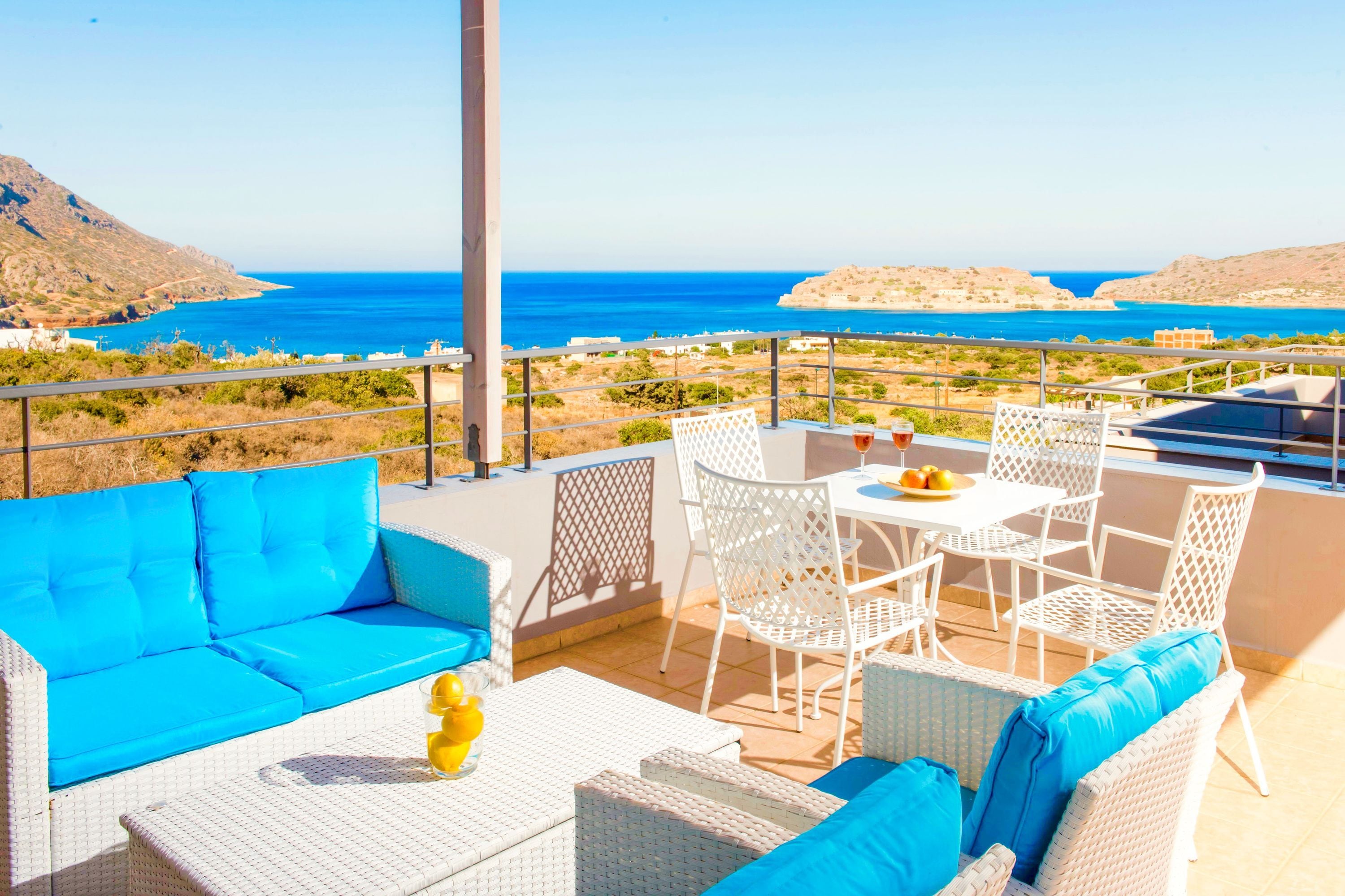 A terrace with a blue sofa, white wicker furniture, and a table with a fruit bowl and glasses.