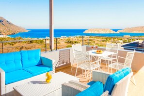 A terrace with a blue sofa, white wicker furniture, and a table with a fruit bowl and glasses. - Venus in Agios Nikolaos (Agios Nikolaos)