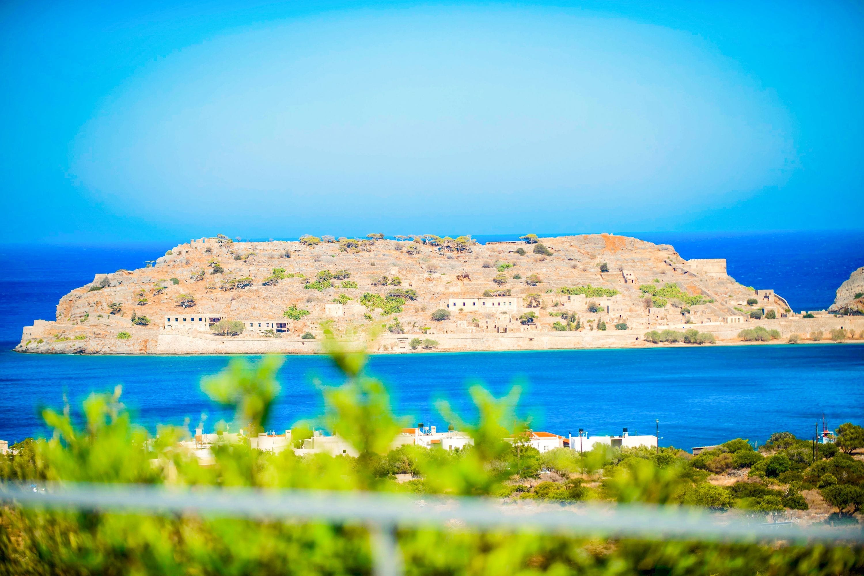 Un paysage côtier avec une colline, une mer bleue et limpide, et des bâtiments.