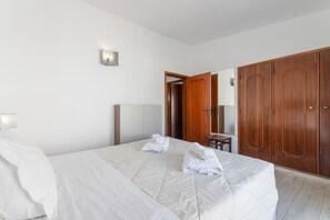 A hotel room with a bed, a wooden wardrobe, a small table, and a mirror. - Apartment 'Apartamento Boa Vista' with Sea View, Balconies and Wi-Fi in Albufeira (Albufeira)