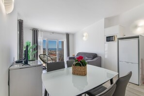 Eine moderne Küche mit weißen Geräten, einem Esstisch mit Stühlen, Blick ins Freie und einem Balkon mit einer Sitzecke.