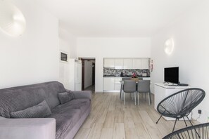 A modern living room with a grey sofa, a dining area with a table and chairs, and a kitchen with white cabinets and a black TV. - Apartment 'Apartamento Boa Vista' with Sea View, Balconies and Wi-Fi in Albufeira (Albufeira)
