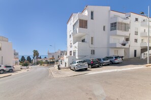 A residential street with white buildings, parked cars, and a clear view of the sea in the background. - Apartment 'Apartamento Boa Vista' with Sea View, Balconies and Wi-Fi in Albufeira (Albufeira)