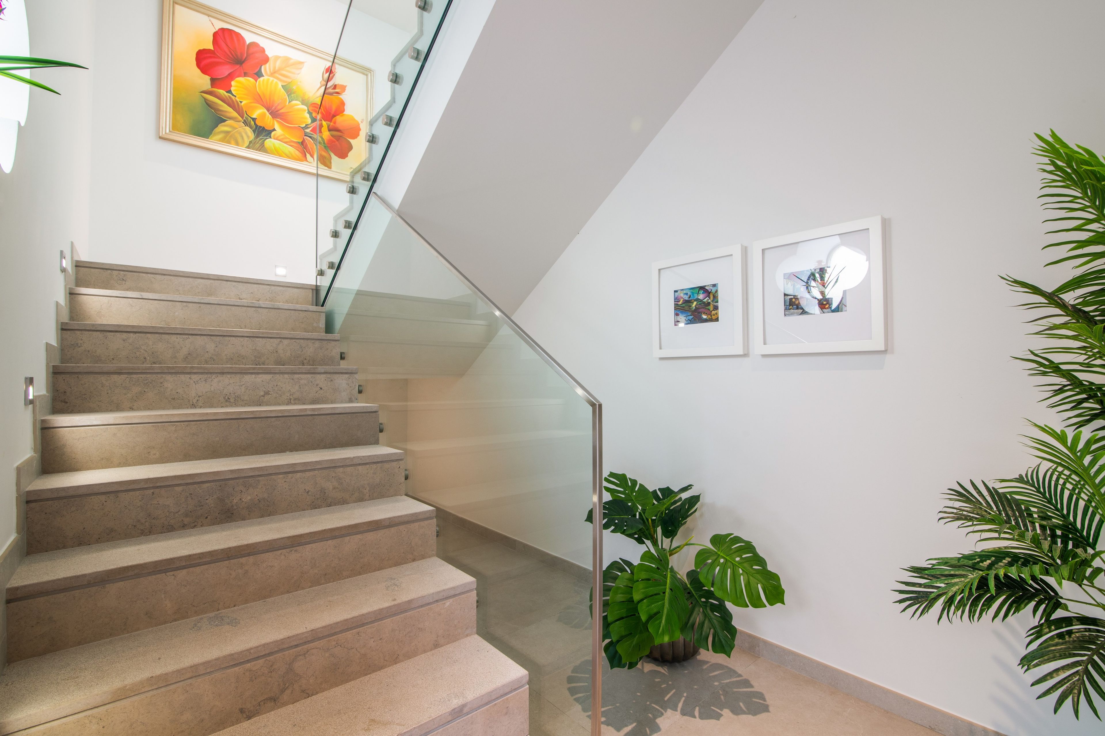 Escadaria com corrimão de vidro que leva a um patamar onde duas obras de arte emolduradas estão expostas.