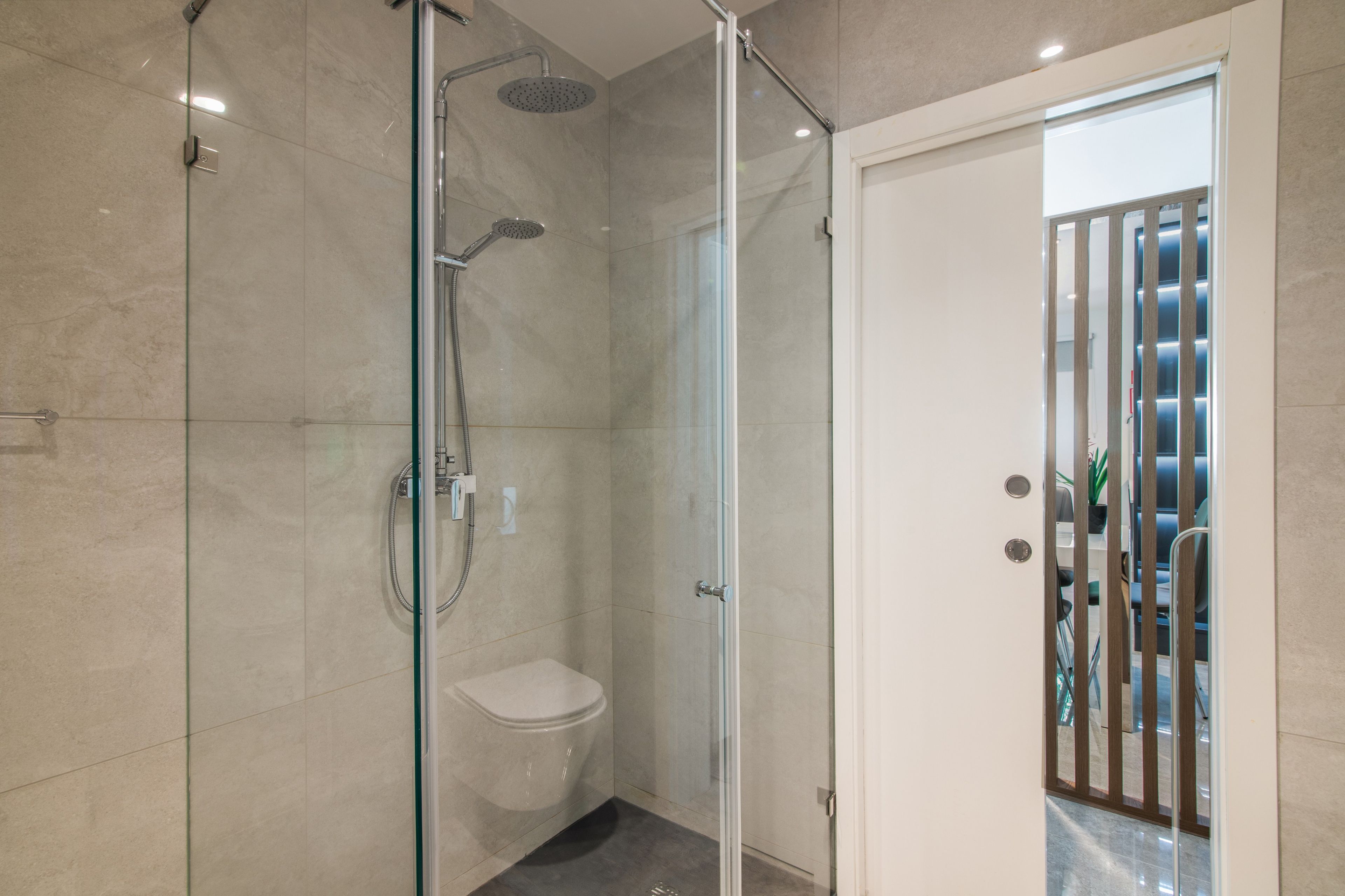 A modern bathroom with a glass-enclosed shower, a toilet, and a door leading to a seating area with a view.