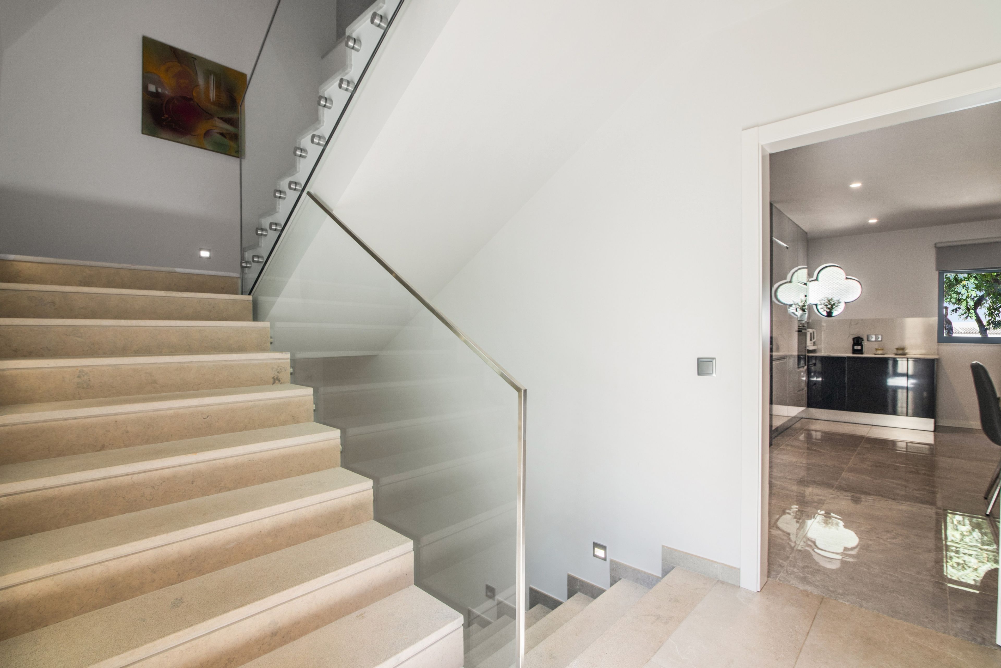 Un escalier avec une rampe en verre menant à un espace cuisine moderne.
