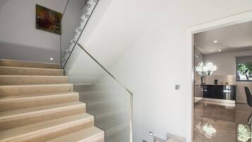 Un escalier avec une rampe en verre menant à un espace cuisine moderne.