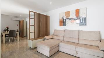 A modern living room with a sectional sofa, a dining area with chairs, and a wall-mounted air conditioner.